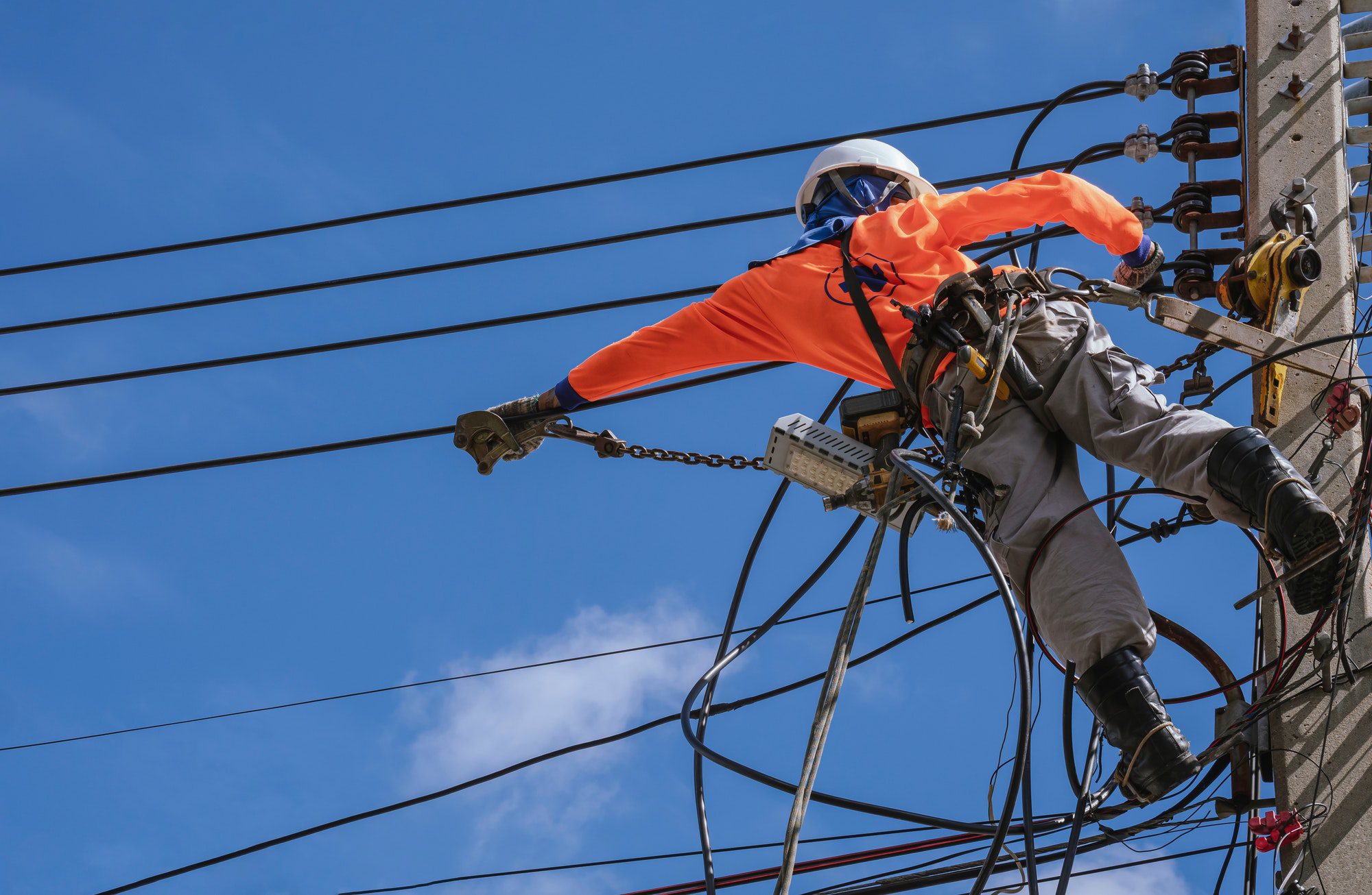Electrician with work tools is installing cable lines and electrical system on power pole